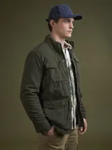 Campera verde militar con cuello alto, cierre frontal con cremallera y botones a presión, múltiples bolsillos con solapa y puños ajustables.