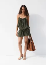 Vestido corto verde militar de diseño recto, con escote recto, tirantes finos y volantes en capas. Cuenta con forro interior.