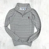 Buzo gris a rayas horizontales blancas y negras, con cuello alto y cierre metálico a la altura del pecho.