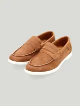 Mocasín tipo penny loafer confeccionado en gamuza marrón, con suela blanca de goma y detalle de antifaz en el empeine.
