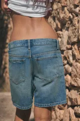 Bermuda de tiro medio confeccionada en denim de color negro gastado, con diseño de cinco bolsillos, trabillas para cinturón y cierre frontal con cremallera y botón metálico.