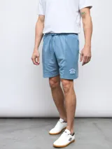 Bermuda deportiva de felpa sin friza, color celeste claro con efecto lavado. Presenta cintura elástica con cordón de ajuste y logo Umbro bordado en la pierna derecha.