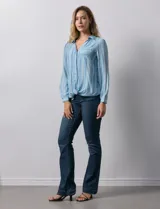 Camisa de gasa celeste con estampado de rayas verticales en tonos azules, rosas y verdes. Tiene cuello con solapa, escote en V, abertura central con botones, bolsillo aplicado en el pecho y terminación anudada en la parte delantera.