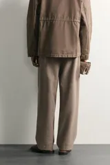 Pantalón relaxed fit de hombre color marrón con textura estructurada, cintura con pliegues frontales, bolsillos laterales y cierre frontal con cremallera y botón.