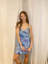 Vestido corto de tela metalizada en tono fucsia con reflejos dorados, con escote en V, diseño de top con triángulos, aberturas laterales en la cintura y doble volado irregular en el ruedo.