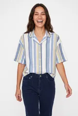 Camisa de manga corta a rayas verticales en tonos azul, amarillo y blanco, con cuello solapa y cierre frontal de botones.