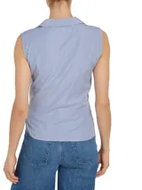 Blusa sin mangas con cuello camisero, diseño cruzado con lazo en la cintura y estampado a rayas verticales azules y blancas.
