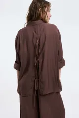 Camisa color marrón de corte oversized, con abotonadura frontal y en las mangas. Presenta un corte vertical en la espalda con lazos decorativos.