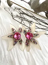 Aros con diseño de flor, compuestos por pétalos en color crema y un centro decorado con cristales en tonos rosados.