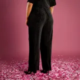 Pantalón de corte ancho y fluido, confeccionado en tejido de terciopelo con textura acanalada. Presenta un diseño de tiro alto con cintura elástica y caída recta.