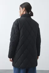 Campera capitoneada de largo medio, color negro, con cuello alto, cierre frontal con cremallera y broches a presión, y bolsillos laterales con solapa.