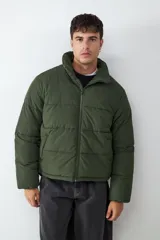 Campera puffer de color verde militar con cuello alto, cierre frontal de cremallera y bolsillos laterales funcionales.