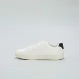 Zapatillas blancas de cuero sintético con cordones, suela plana y detalle de refuerzo negro en el talón.