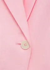 Chaqueta de lino color rosado, con diseño recto, cuello con solapas de muesca y cierre frontal de un botón. Cuenta con mangas largas con puños abotonados, dos bolsillos de ribete delanteros y abertura posterior en el bajo.