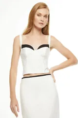 Falda midi color blanco con corte recto, abertura lateral y ribete negro en cintura, ruedo y abertura.