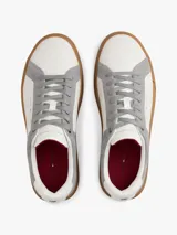 Zapatillas de tenis Tommy Hilfiger de corte bajo, confeccionadas en piel nobuk con paneles de texturas mixtas en blanco y gris. Presentan suela de goma color caramelo, cierre con cordones y detalles distintivos de la marca en la lengüeta, lateral y talón.