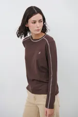 Remera de manga larga color marrón chocolate, con costuras decorativas en contraste de color blanco a lo largo de las mangas y el cuello. Presenta un pequeño logo bordado en el pecho.