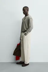 Camiseta de manga larga con cuello panadero (henley) y cierre de tres botones. Presenta un patrón de rayas horizontales finas en tonos beige y negro, con pespuntes a contraste en el cuello, puños y bajo.