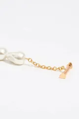 Pulsera de cadena de eslabones dorados combinada con perlas barrocas. Cuenta con un cierre de barra en T y dos dijes colgantes en forma de corazón, uno metálico y otro esmaltado en color rojo con el logo de la marca.