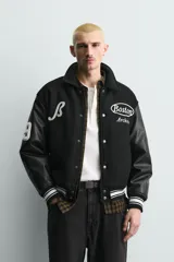 Cazadora estilo varsity con cuerpo de tejido con lana y mangas de efecto piel. Presenta cuello solapa, cierre frontal con botones a presión, bolsillos laterales y puños con elástico a rayas. Incluye parches y bordados decorativos en el frente.