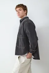 Sobrecamisa de denim en color negro lavado, con cierre frontal de botones metálicos, cuello clásico y un bolsillo de parche en el pecho. Presenta costuras a la vista y puños abotonados.