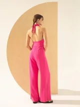 Mono fucsia con escote halter, espalda descubierta, lazo en la cintura y pantalón palazzo con tajos laterales.