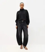 Pantalón baggy balloon de jean negro, de tiro medio con bolsillos delanteros y traseros, recortes estructurales y botamanga ajustada. Incluye cinto de poliuretano con hebilla metálica.