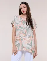 Blusa de silueta holgada confeccionada en crepé liviano, con estampado abstracto en tonos rosados, verdes y blancos. Presenta escote redondo amplio, hombros caídos con hilera de botones decorativos, mangas cortas con dobladillo y ruedo asimétrico en picos.