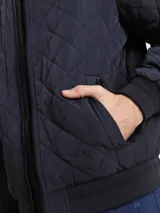 Campera estilo bomber acolchada de color azul marino, con patrón de costuras en rombos. Presenta cierre frontal de cremallera, cuello, puños y dobladillo en punto canalé oscuro. Incluye bolsillo utilitario con cremallera en la manga izquierda con cinta con el logo de Calvin Klein.