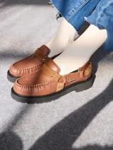 Mocasines Mutma Gales de cuero color tostado, con plataforma gruesa dentada, detalles de tachas metálicas, argollas y tira lateral con hebilla.