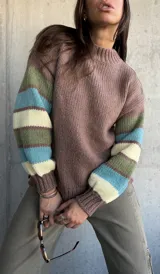 Sweater de tejido de punto con cuerpo en color marrón y mangas con diseño de rayas horizontales en tonos verde, turquesa y crema. Presenta cuello redondo y puños acanalados.