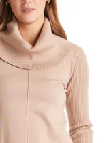 Buzo de punto color beige con cuello volcado amplio, mangas largas acanaladas y torso liso. Presenta una costura central vertical, ruedo con tajos laterales y largo asimétrico, siendo más largo en la parte posterior.