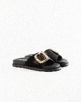 Sandalias de cuero color negro, de diseño plano con una tira ancha en el empeine y una hebilla metálica dorada grande como detalle.