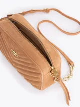 Bandolera de gamuza gris con diseño matelaseado en forma de V. Presenta un aplique metálico dorado en forma de labios en el frente y una correa combinada con cadena metálica dorada.