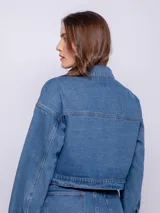 Campera corta de jean color blanco, con cuello camisero, botones metálicos plateados en el frente y puños, y bolsillos delanteros con solapa.