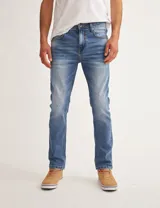 Pantalón de jean azul de corte slim fit, con lavado medio y detalles de desgaste.
