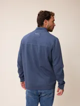 Buzo de cuello alto con cierre frontal completo, confeccionado en tejido de algodón y poliéster. Presenta un diseño liso en color azul melange con un pequeño logo bordado en el pecho y bolsillos laterales.