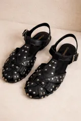 Sandalias tipo guillermina negras con tiras trenzadas y tachas plateadas. Cierre de hebilla en el tobillo.