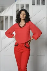 Blusa corta color rojo con cuello redondo y mangas largas abullonadas. Presenta detalle de apliques de pedrería en el cuello y en los bolsillos frontales.