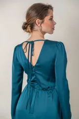 Vestido largo de fiesta en satén de seda color petróleo, con escote en V profundo, mangas largas y falda cruzada con abertura. Presenta aplique de strass en la cintura.