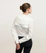 Campera rompevientos deportiva cropped de color blanco, con capucha, cierre frontal y puños elásticos. Confeccionada en poliamida, presenta un diseño ligero y funcional.