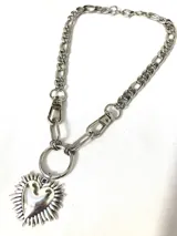 Collar de acero quirúrgico con cadena de eslabones y dije de corazón exornado con rayos, sujeto por una argolla con mosquetones.