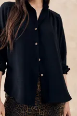 Blusa negra con cuello mao, calce al cuerpo y mangas 3/4 con puños abotonados. Cierre frontal con botones.