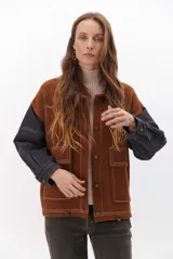 Campera color caramelo con mangas de denim azul oscuro. Presenta cuello alto, cierre frontal con botones, cuatro bolsillos delanteros con solapa y pespuntes blancos decorativos.