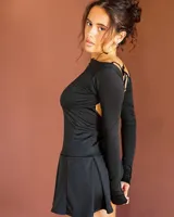 Vestido corto negro de manga larga, con diseño ajustado al cuerpo y falda tableada. Presenta una espalda descubierta con detalle de tiras cruzadas.