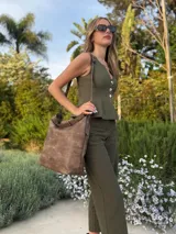 Cartera tipo bandolera de gran tamaño, confeccionada en cuero sintético con acabado desgastado. Cuenta con una asa corta fija, una correa larga regulable y extraíble, y una placa metálica con la marca en la parte frontal.