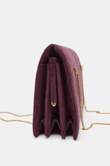 Bolso de hombro rígido de piel color bordó, con diseño de pespuntes, triple compartimento y cierre magnético. Cuenta con doble asa de cadena metálica dorada.