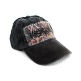 Gorra tipo dad hat de color negro con efecto lavado, que presenta un parche rectangular con estampado de camuflaje tipo Realtree y bordado en estilo metal, unido a la gorra mediante costuras visibles en hilo blanco.