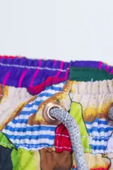 Short de baño con estampado de aguacates, tomates, limones, botellas de salsa picante y tragos de tequila sobre un fondo de rayas horizontales azules y blancas.