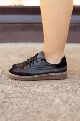 Zapatillas urbanas negras de cuero con detalles en gamuza y suela marrón con costuras blancas.